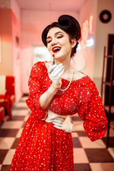 Sexy pin up woman with bright lipstick in hand sitting against mirror, dress with polka dots, vintage style. Retro cafe 50 american fashion