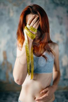 Skinny woman covers her face with hands tied in measuring tape. Fat or calories burning concept. Weight loss, anorexia