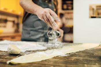 Male person in apron preparing dough on wooden kitchen table. Homemade pasta cooking process