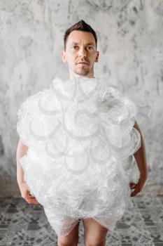 Funny freak man wrapped in packaging film, grunge room interior. Mad male person in abandoned house, crazy guy