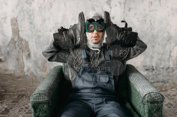 Funny freak man in swimming goggles wearing shoes on his hands, grunge room interior. Nerd in abandoned house, crazy guy