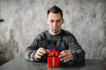 Autistic man sitting against gift in wrapping paper. Alone guy in abandoned house, autism syndrome