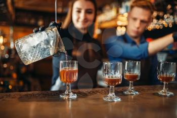 Male and female bartender at the bar counter. Alcohol drink preparation. Two barmans working in pub