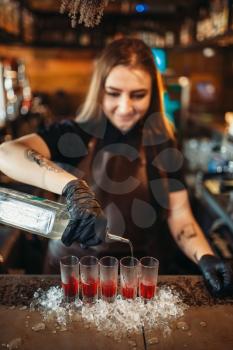 Female barman in gloves pours beverage into a glass. Woman bartender mixing at the bar counter in pub. Barkeeper occupation