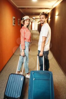 Smiling couple with suitcase in hotel hallway. Travelling or tourism concept. Travelers with bags in corridor