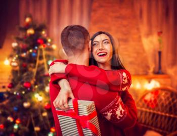 Happy love couple hugs, christmas holidays. Xmas celebration, cheerful man and woman with gift, fir-tree with decoration on background