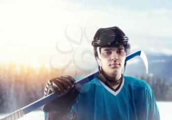 Portrait of ice hockey player in helmet and equipment, snowy forest on background. Ice-skating outdoors. Winter season men sport
