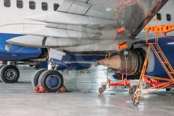 Passenger jet airplane in hangar, plane on inspection before flight. Aircraft on repairing, fixing the problem, engine maintenance, troubleshooting, air transportation safety
