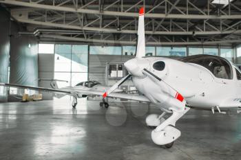 Small private turbo-propeller airplane in hangar, plane on inspection before flight. Air transportation, front view on turboprop plane