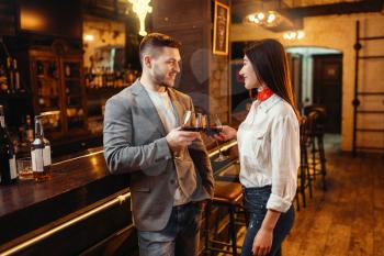 Man and woman drinks red wine at wooden bar counter. Couple leisures in pub, husband and wife relaxing together in nightclub