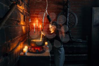 Scary witch cooking soup and reads spell, dark powers of witchcraft, spiritual seance with candles. Female foreteller calls the spirits, terrible future teller