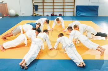 Young boys in kimono makes push up exercise, kid judo. Young fighters in gym, martial art