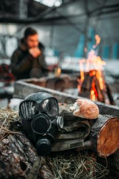 Gas mask against fire, stalker eats on background. Post apocalyptic lifestyle, doomsday, horror of nuclear war