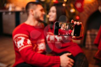 Love couple makes selfie on phone camera, romantic xmas celebration. Christmas holidays, man and woman happy together, festive decoration on background