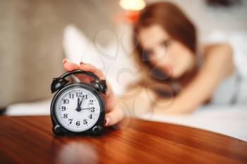 Female person hand on alarm clock, waking up. Morning bedding at home, relaxation in bedroom