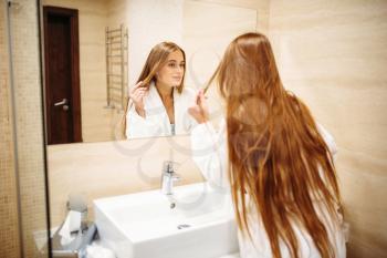 Beautiful woman in bathrobe against mirror in bathroom, morning hygiene, beauty and hair care