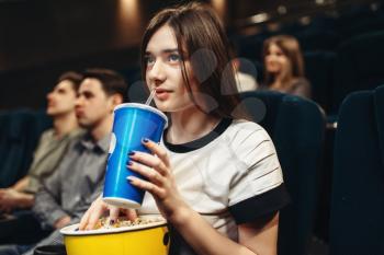 Young woman with beverage and popcorn sitting in cinema. Showtime, movie watching