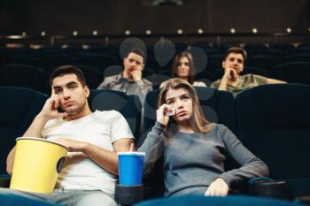 Man and woman with popcorn in cinema. Boring film concept, couple watching movie
