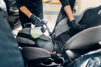 Professional dry cleaning of car interior. Carwash service, male worker in gloves using spray