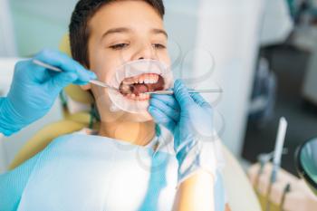Little boy with open mouth in a dental cabinet, caries removal procedure, pediatric dentistry. Female dentist looking for caries