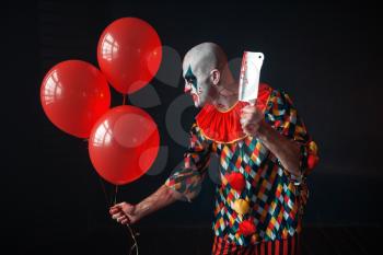 Scary bloody clown with meat cleaver and air balloon sneaking into the basement, horror. Crazy maniac
