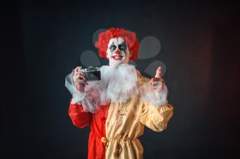Scary bloody clown with crazy eyes makes picture. Man with makeup in carnival costume, mad maniac