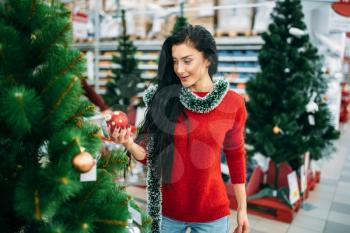 Young woman looks on christmas tree toy in supermarket. December shopping, choosing of holiday decorations