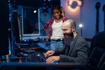 Sound engineer and female singer at remote control panel in audio recording studio. Musician in headphones listens composition, professional music mixing