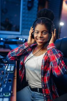 Female musician in headphones at the remote control panel in audio recording studio. Sound engineer at the mixer, professional music mixing
