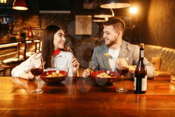 Couple at wooden bar counter, romantic dinner with red wine. Lovers leisures in pub, husband and wife relaxing together in nightclub