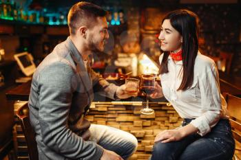Love couple relaxing with alcohol at wooden bar counter, romantic evening. Lovers leisures in pub, husband and wife relaxing together in nightclub