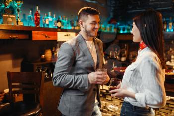 Love couple with alcoholic beverages talking at bar counter, romantic evening of man and woman. Lovers leisures in pub, husband and wife relaxing together in nightclub