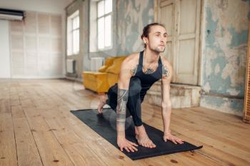 Male yoga with tattoo on hand doing exercise in gym with grunge interior. Fitness training indoors
