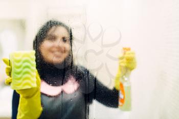 Maid in gloves cleans glass with a cleaning spray, hotel bathroom interior on background. Professional housekeeping, charwoman
