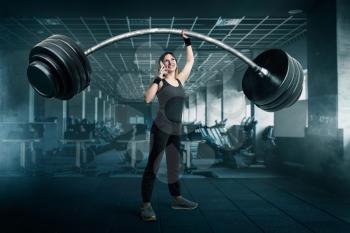 Female athlete with very big barbell talking by phone on workout in gim. Woman with weights, weightlifting sport concept