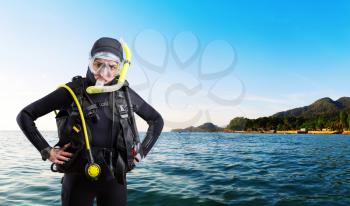 Female diver in wetsuit and diving gear, ocean shore on background. Frogman in mask and scuba on the beach. underwater sport