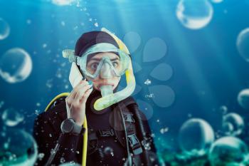 Diver in wetsuit speaks on phone, underwater view. Frogman in mask and scuba swims in the ocean