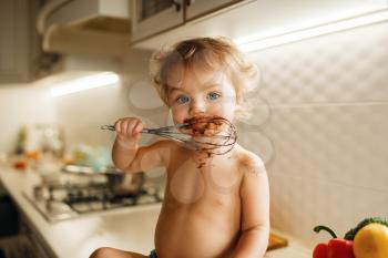 Female kid tastes melt chocolate, pastry preparation. Cute little girl cooking on the kitchen. Happy child prepares sweet dessert at the counter