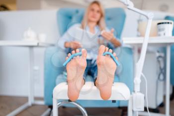 Beautician salon, foot care procedure. Legs treatment for female client in beauty shop, customer sitting in armchair, relaxation before pedicure