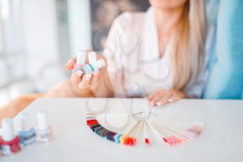 Female customer holds nail varnish bottles, colorful palette on the table in beauty shop. Professional manicure and pedicure service, beautician salon, woman at the manicurist
