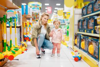 Mother with little daughter in kids store. Mom and child together choosing toys in supermarket, family shopping