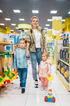 Mother with her little children in kids store. Mom with daughter and son together choosing toys in supermarket, family shopping