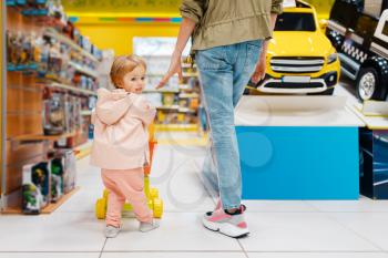 Happy mother with little daughter in kids store. Mom and child together choosing toys in supermarket, family shopping