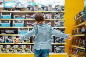 Little boy at the shelf in kids store, back view. Son choosing toys in supermarket, family shopping