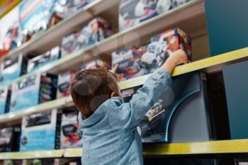 Little boy at the shelf in kids store, side view. Son choosing toys in supermarket, family shopping, young customer buying model