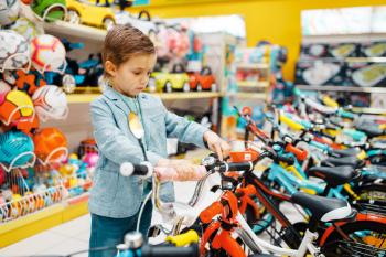 Little boy buying bicycle in kids store, side view. Son choosing toys in supermarket, family shopping, young customer