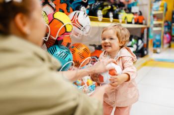 Mother with her little daughter playing with ball in kids store. Mom and child together choosing toys in supermarket, family shopping