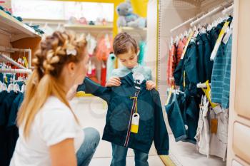 Mother with her little boy choosing clothes in kids store. Mom and child buying jacket in supermarket together, family shopping