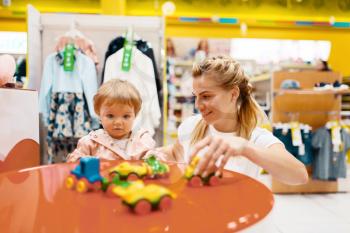 Mother with her little girl playing in kids store. Mom and child buying toys in supermarket together, family shopping
