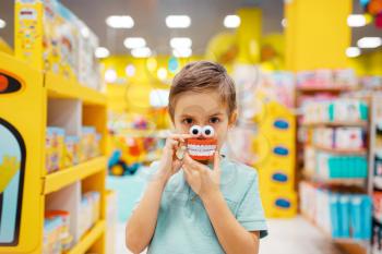 Little boy holds jaw toy at the shelf in kids store, front view. Son choosing toys in supermarket, family shopping, young customer